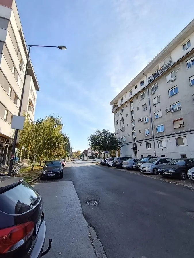 Pogled na ulicu sa parkiranim automobilima ispred stambene zgrade.