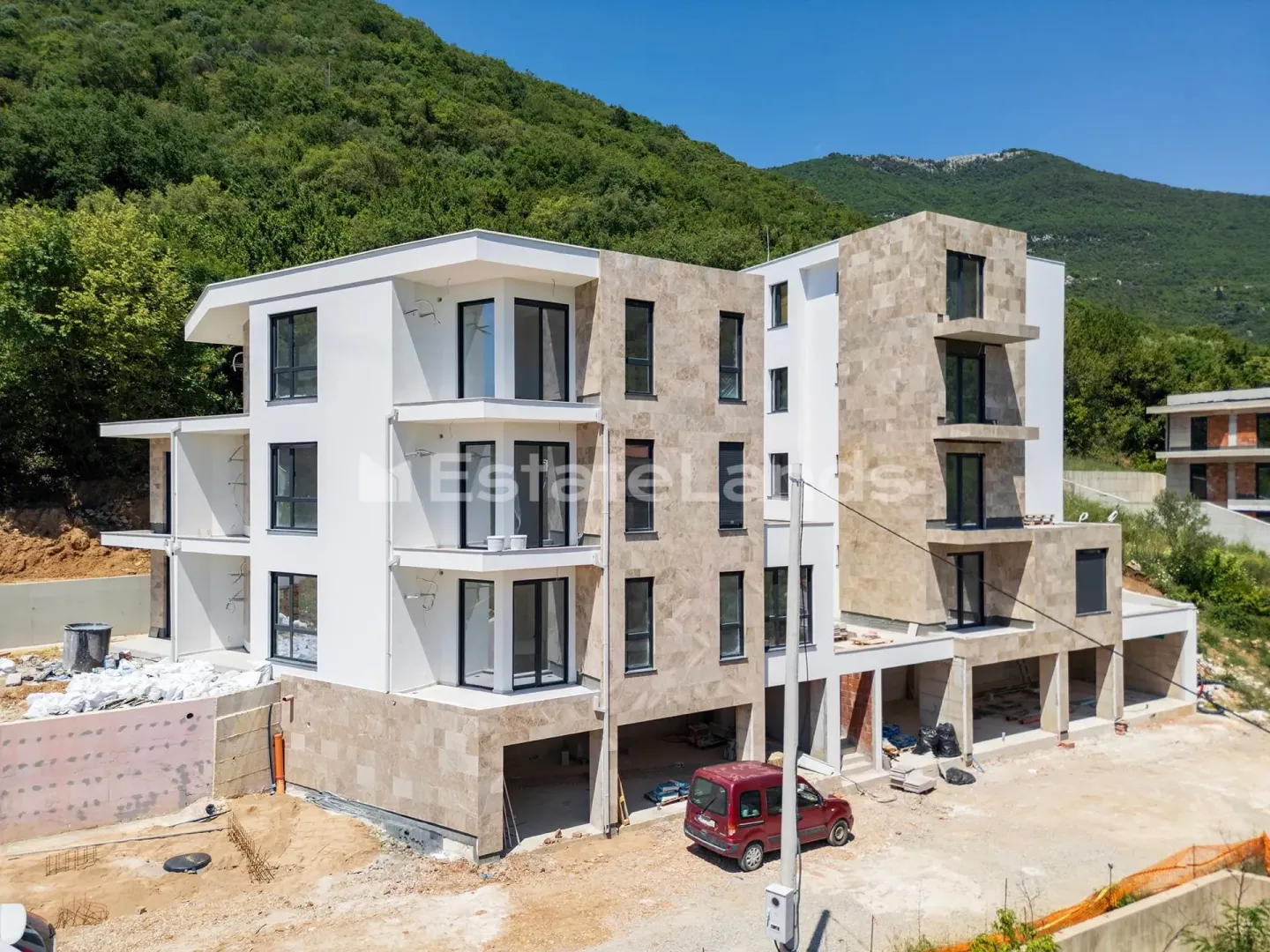 Pogled iz vazduha na višestambenu zgradu u izgradnji sa terasama i kamenom fasadom.