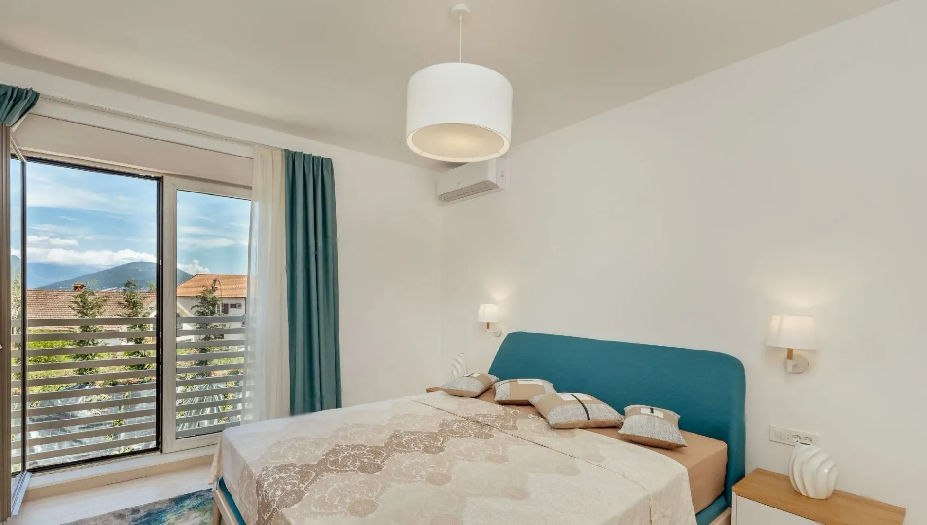 Spavaća soba sa bračnim krevetom, plavim uzglavljem i izlazom na balkon.