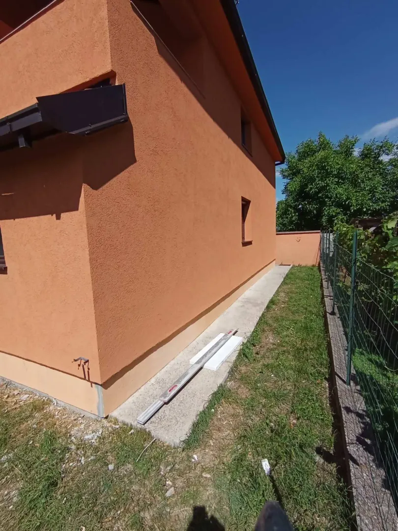 Bočna strana kuće sa narandžastom fasadom i uređenim dvorištem.