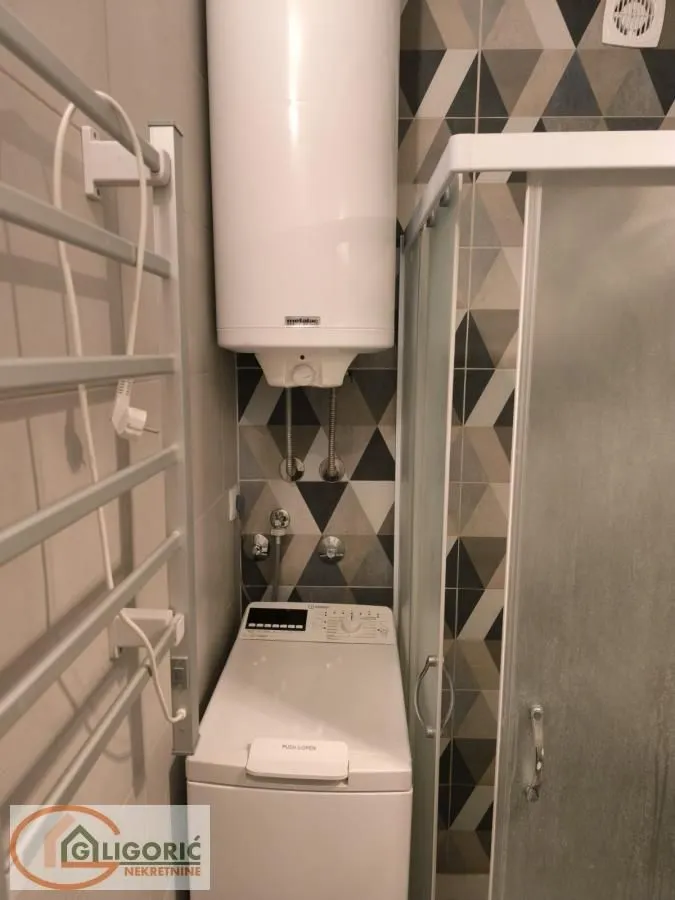 Smaller bathroom with a shower cabin, water heater, and washing machine.