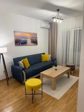 Dnevna soba sa plavom sofom, drvenim stolićem i umetničkom slikom na zidu. - image 3