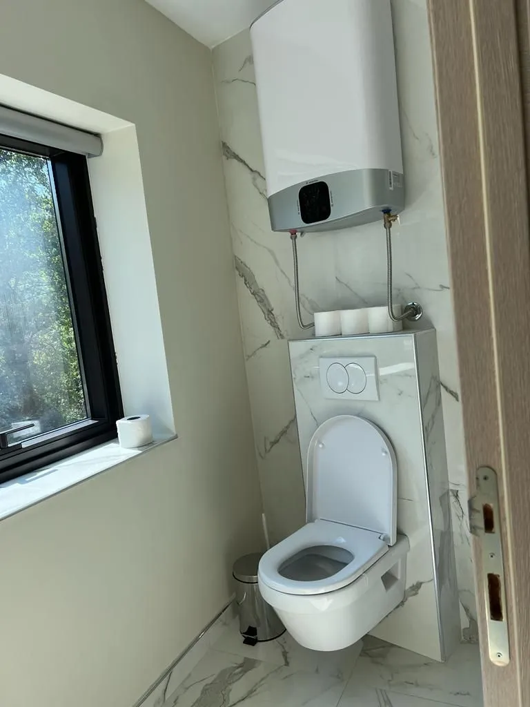 View of the bathroom with a wall-hung toilet and a water heater on the wall.