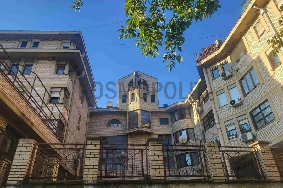 Pogled na spoljašnjost zgrade sa ogradom i drvećem.