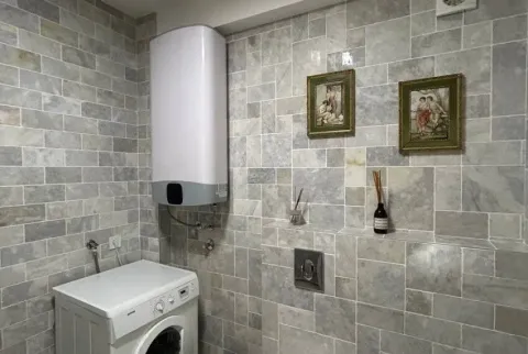 Kupatilo obloženo sivim pločicama sa bagerom, veš mašinom i dekorativnim slikama. - image 4