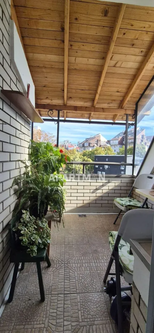 Covered balcony with a wooden ceiling structure and potted flowers.