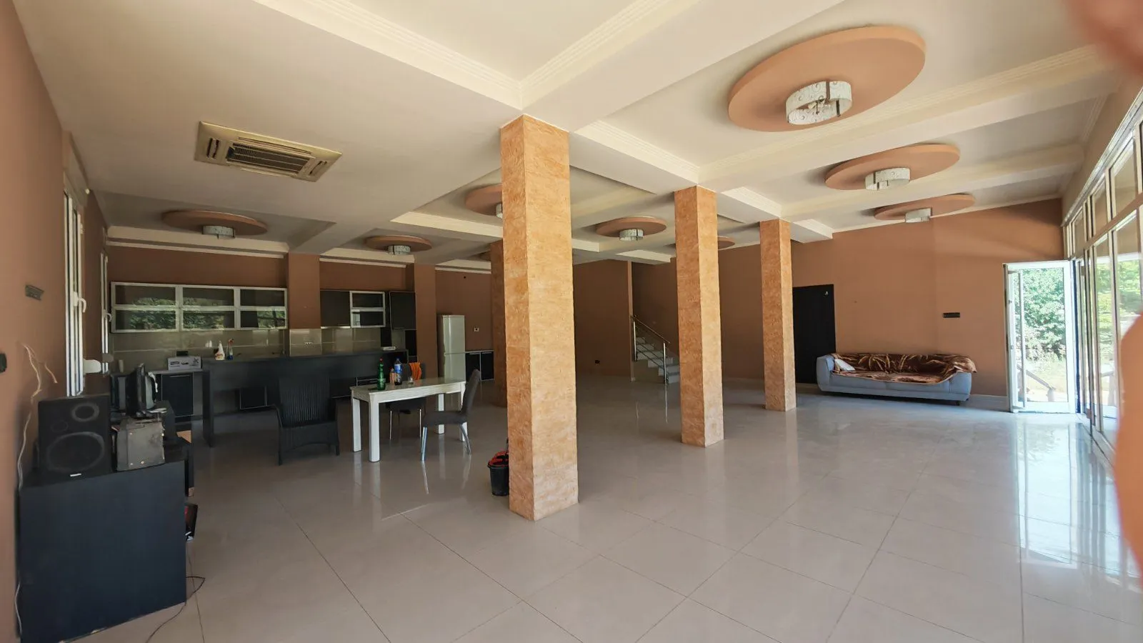 Spacious living room with pillars and a kitchen in the background.