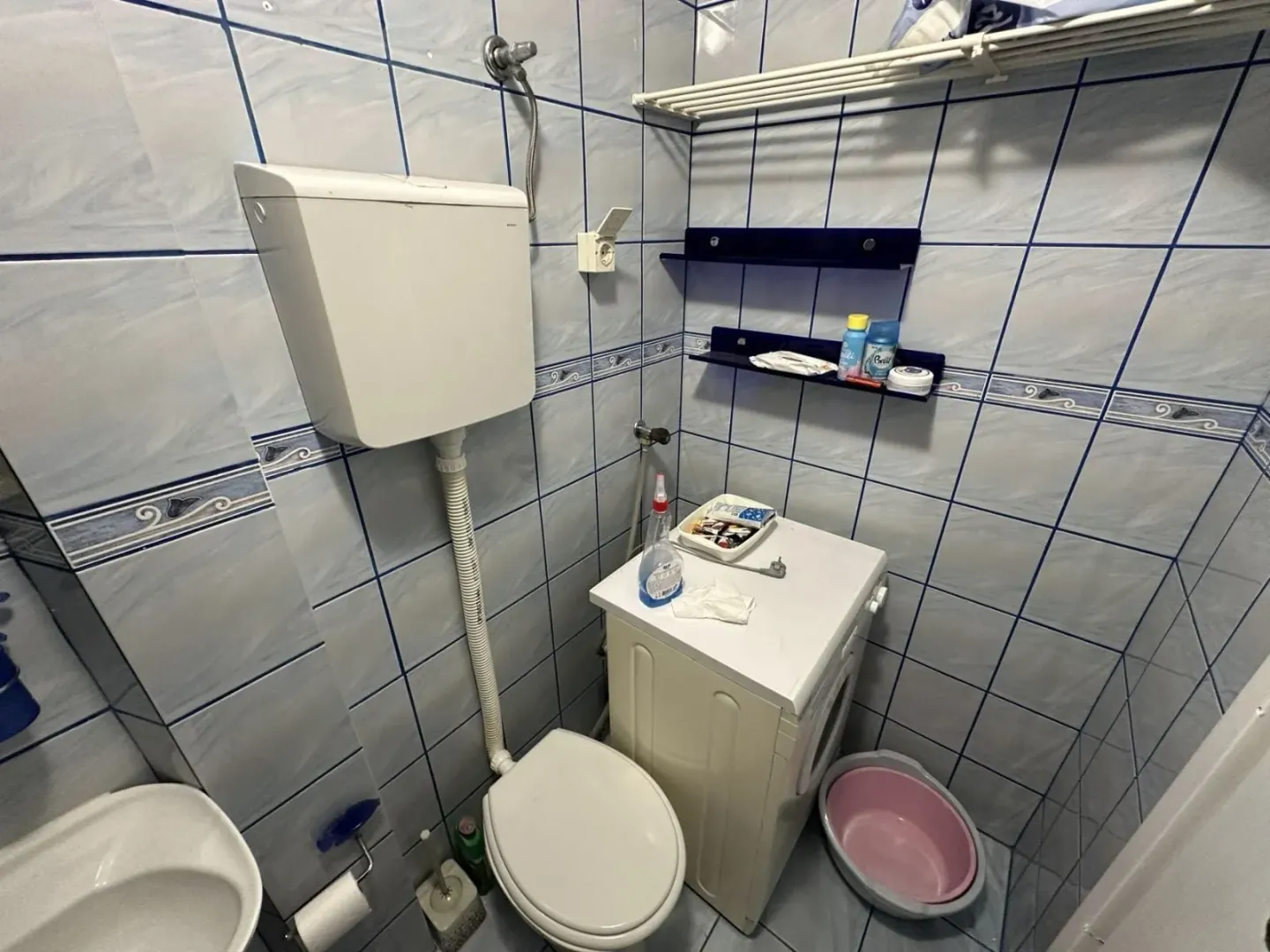 Small bathroom with blue-toned tiles, toilet, and washing machine.