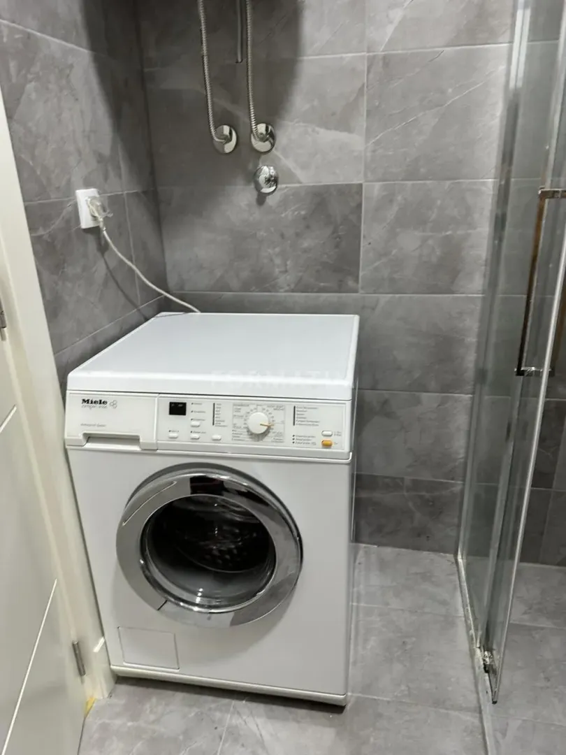 Kupatilo sa veš mašinom i sivim zidnim pločicama.