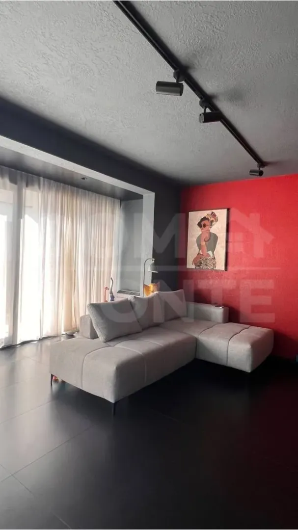 Living room with a sectional sofa, red accent wall, and dark flooring.
