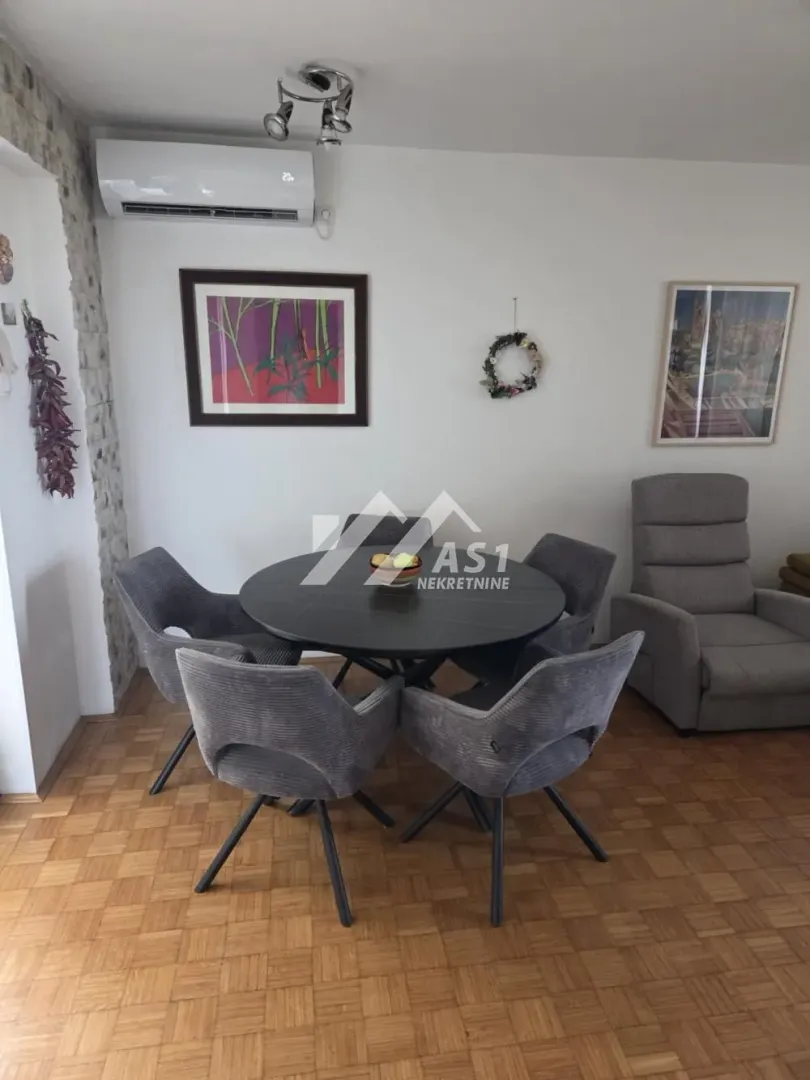 Trpezarija sa okruglim stolom i tapaciranim stolicama u sklopu dnevnog boravka.