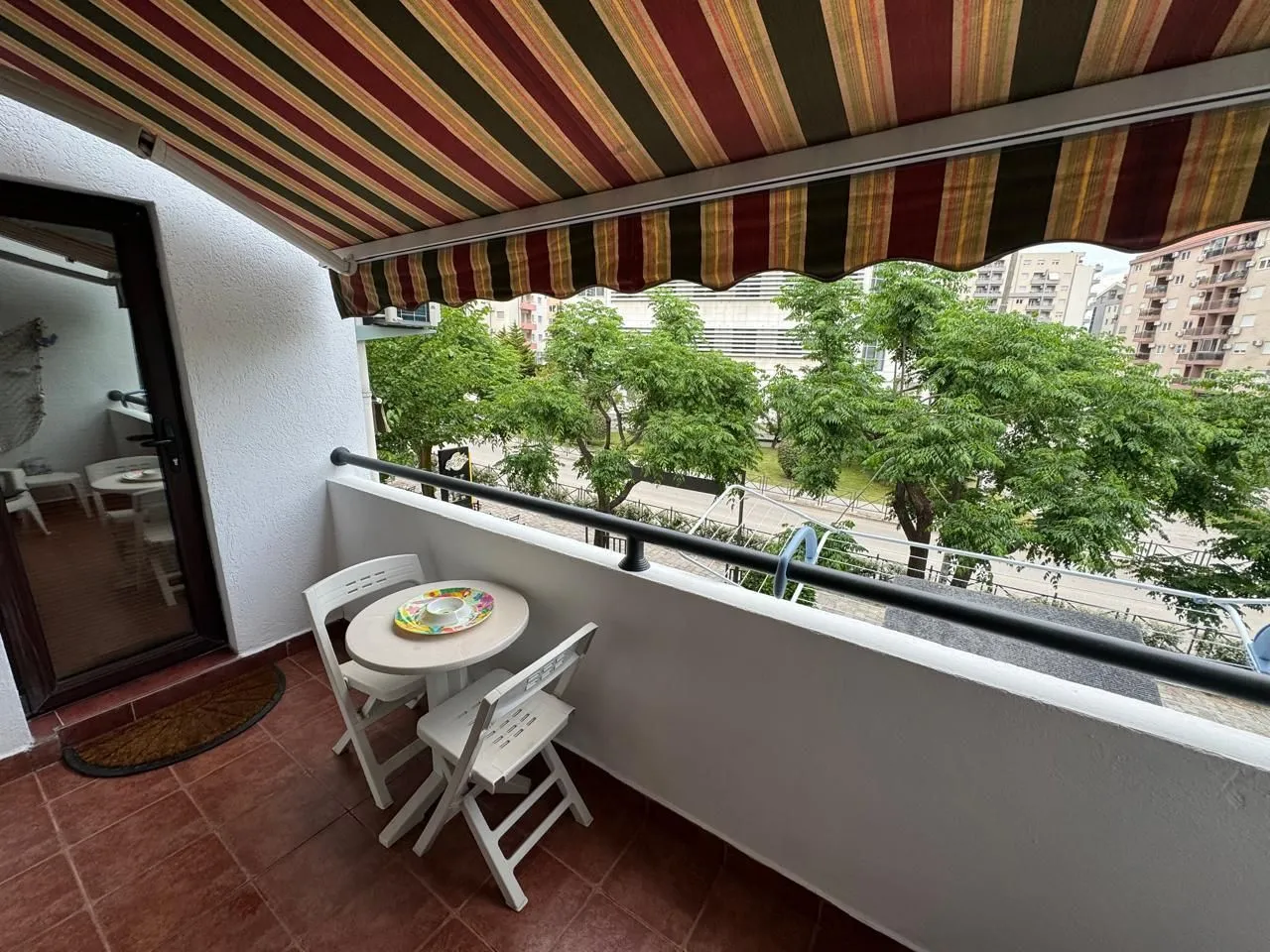 Namješten balkon sa stolom, stolicama i tendom, sa pogledom na zelenilo.