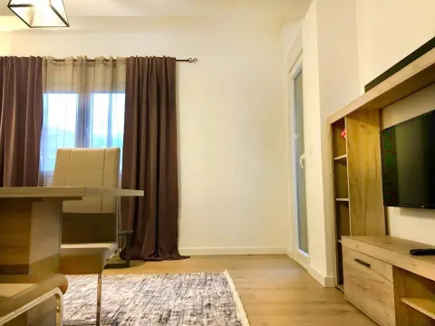 Dnevna soba sa TV policom, trpezarijskim stolom i prozorom sa tamnim zavjesama. - image 3