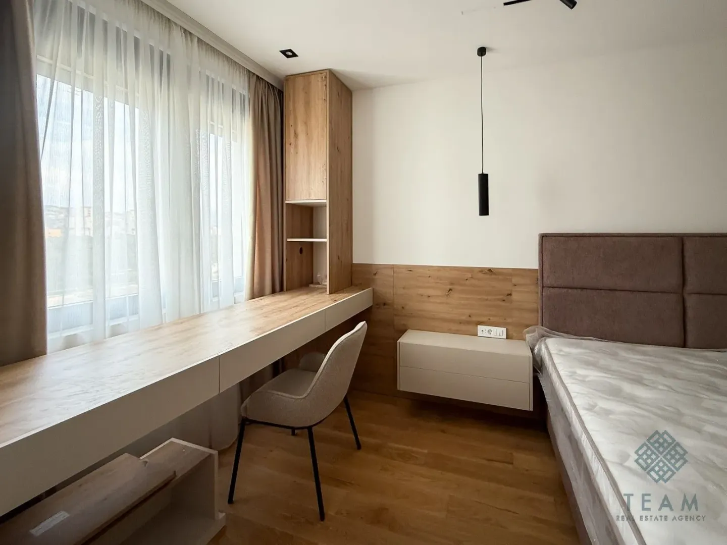 Furnished bedroom with a bed, a desk along the window, and built-in units.
