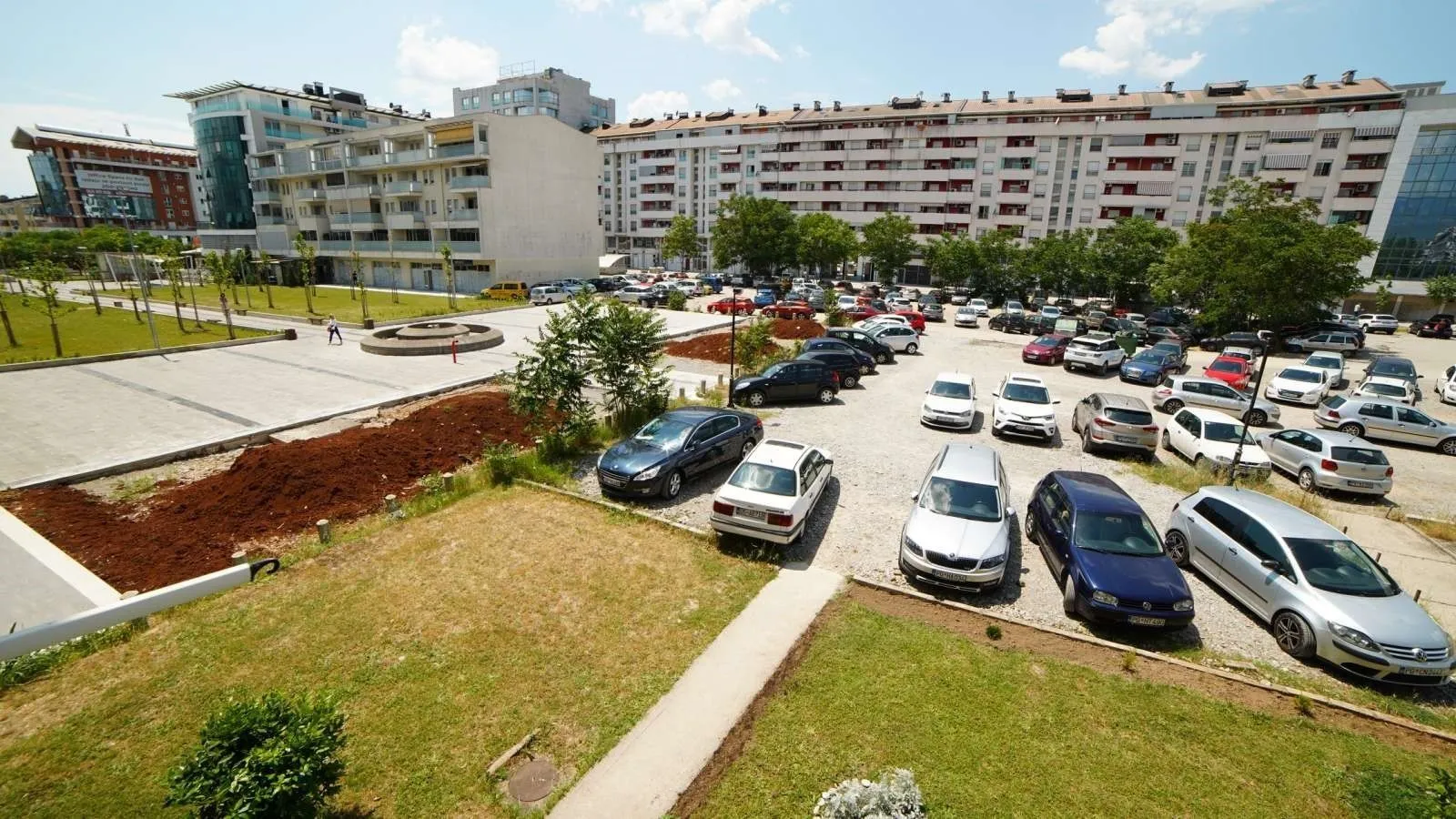 View of a parking lot and surrounding residential buildings from a lawn.