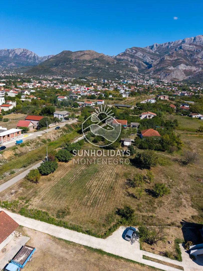 Pogled iz vazduha na plac i okolno naselje sa planinama u pozadini.