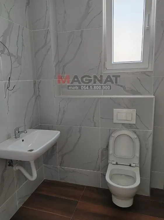 Kupatilo opremljeno umivaonikom, WC šoljom i pločicama sa dezenom mermera.