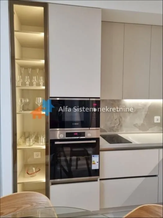 View of a modern kitchen with a built-in oven, microwave, and illuminated glass cabinet.