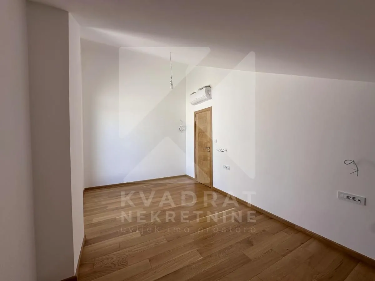 Empty room with wooden flooring, white walls, and a wooden door.