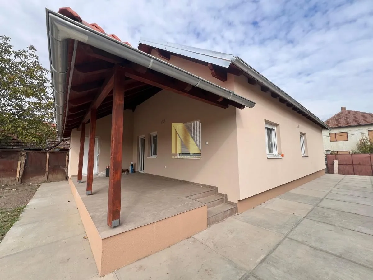 Pogled na spoljašnjost kuće sa natkrivenom terasom i popločanim dvorištem.