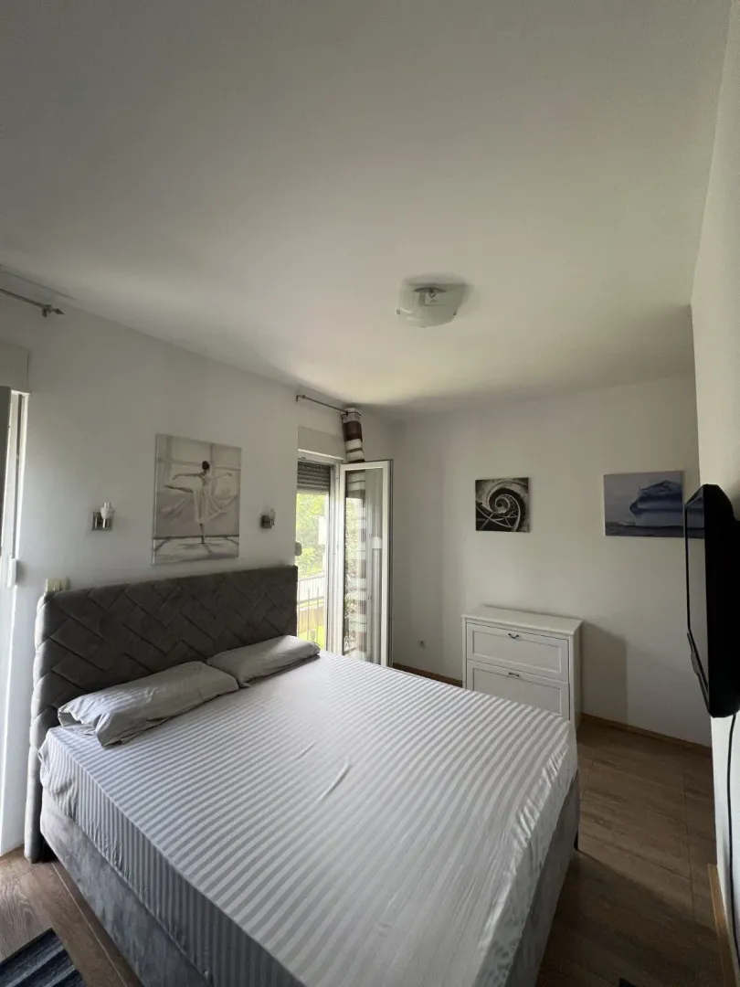 Svijetla spavaća soba sa bračnim krevetom i izlazom na balkon.