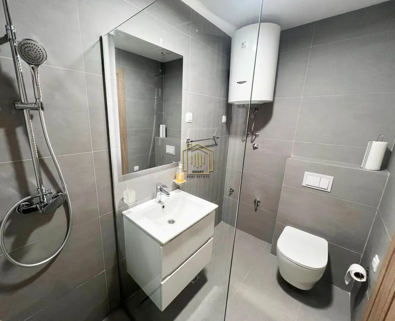 Modern bathroom tiled in gray with a walk-in shower, washbasin, and toilet.