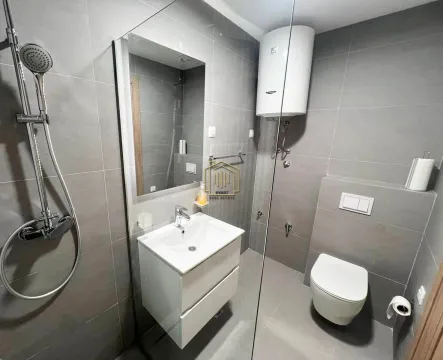 Modern bathroom tiled in gray with a walk-in shower, washbasin, and toilet. - image 3