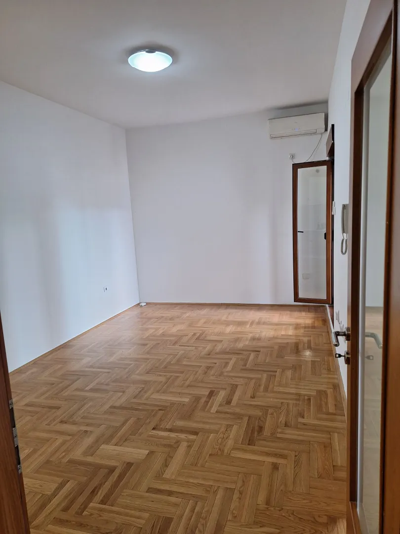 Prazna soba sa parketom i bijelim zidovima.