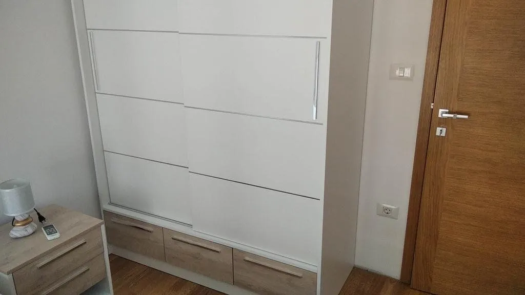 A view of a white wardrobe with sliding doors and wooden details in the bedroom.