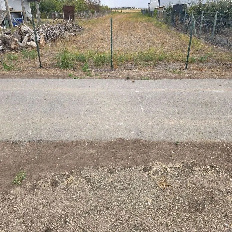 Prikaz parcele sa zemljištem i ogradom pored asfaltnog puta.