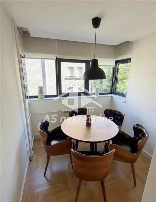 Dining area with a round table and modern chairs by large windows.