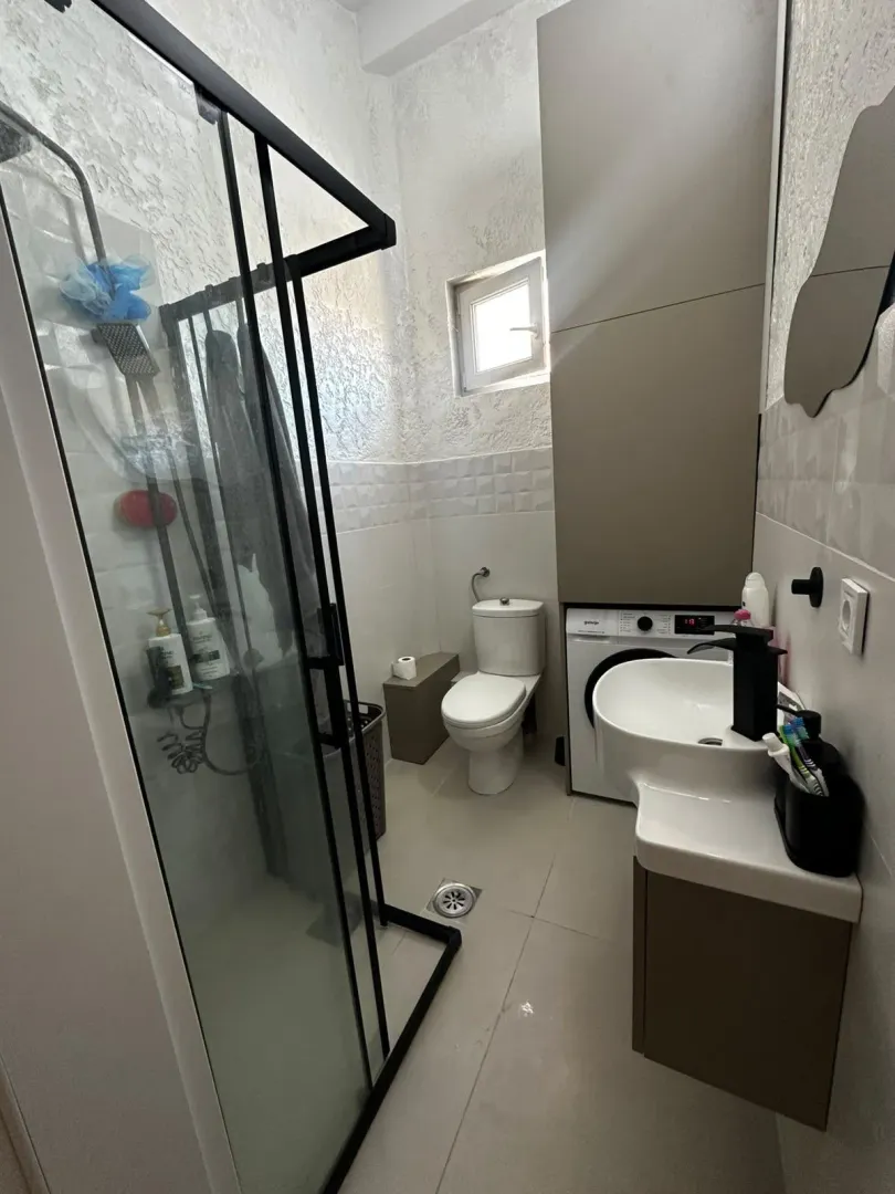 Moderne kupatilo sa tuš kabinom, umivaonikom, veš mašinom i toaletom.