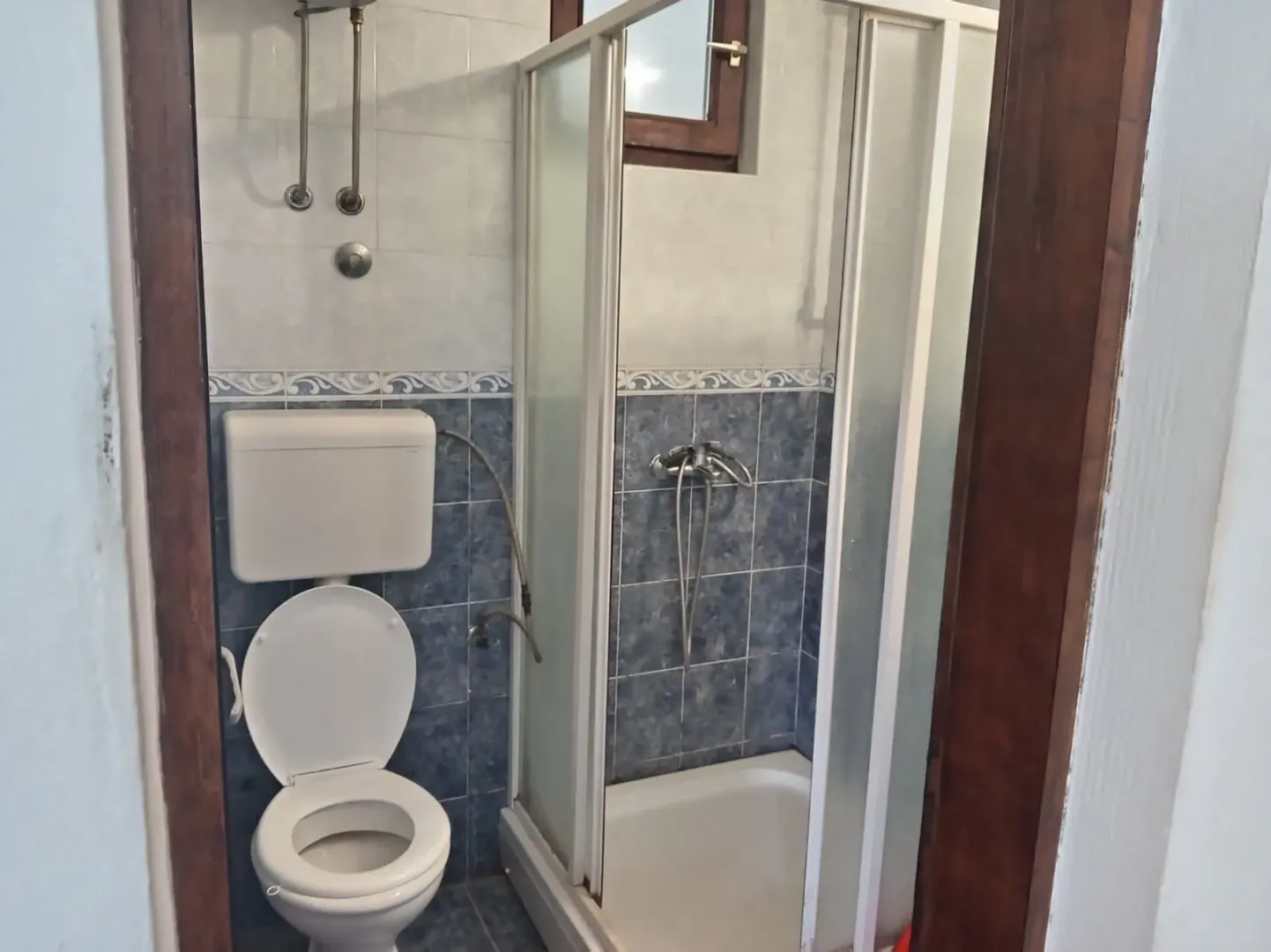 Smaller bathroom with blue tiles, shower cabin and toilet.