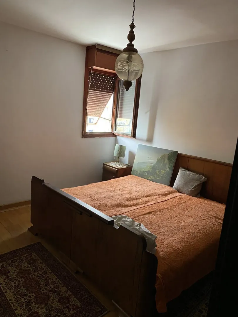 Spavaća soba sa drvenim krevetom i noćnim ormarićem pored prozora.