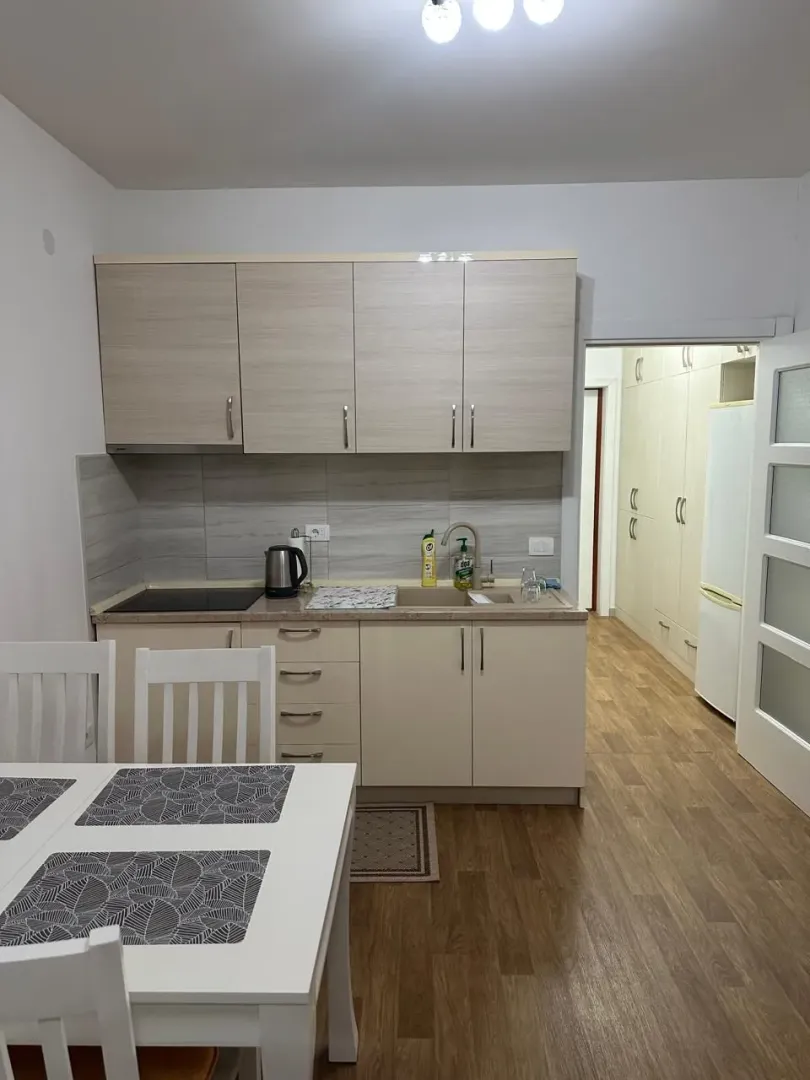 Kuhinja sa elementima u boji drveta i trpezarijskim stolom u prvom planu.