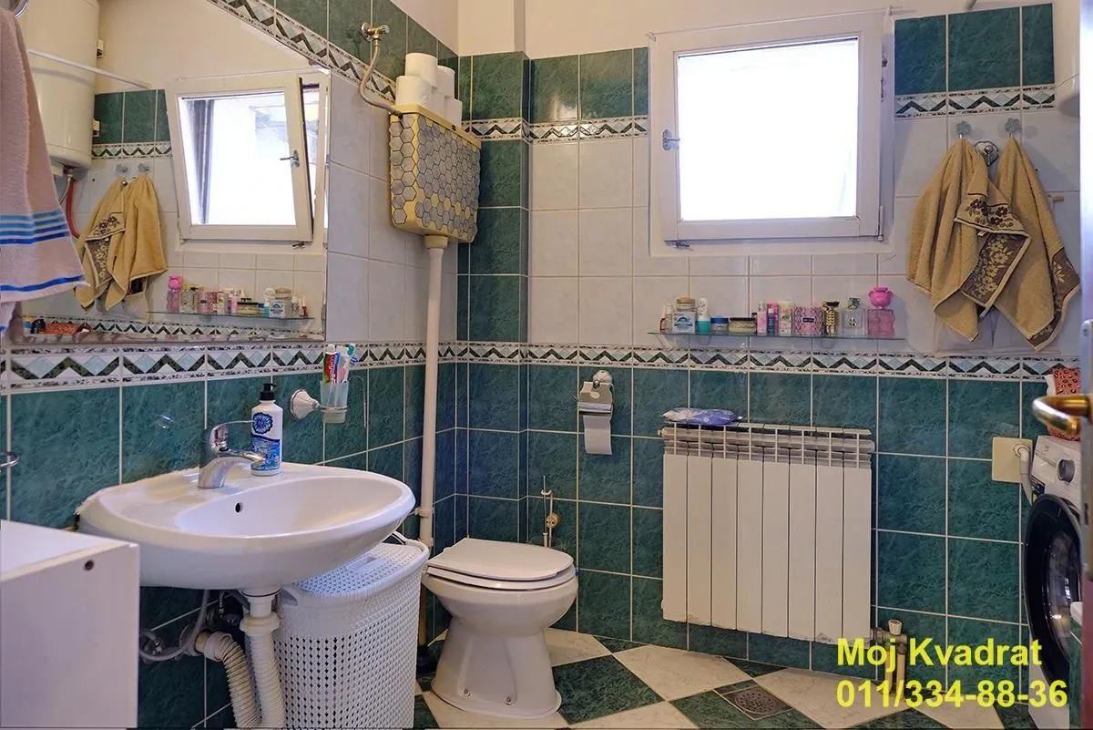 Kupatilo sa umivaonikom, WC šoljom, prozorom i pločicama u zelenim tonovima.