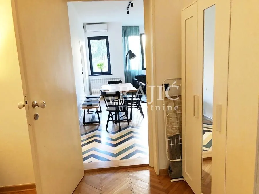 View from the hallway into a bright living room with a dining area and parquet flooring.