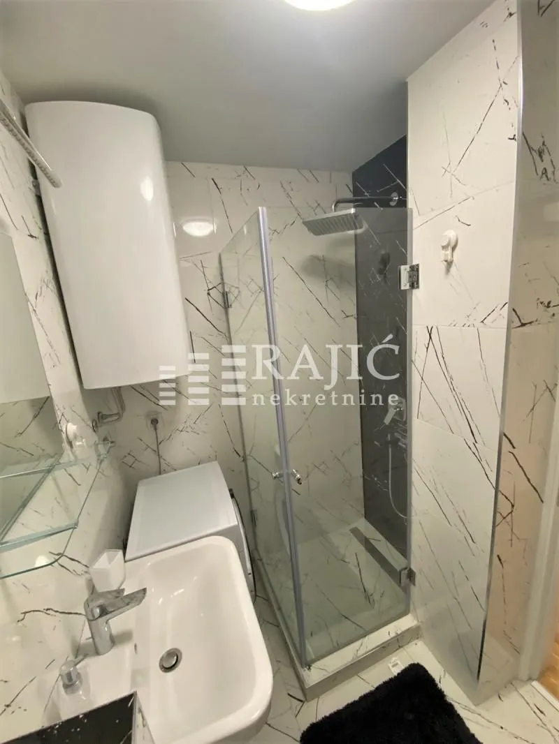 Modern bathroom with a walk-in shower, washbasin, and water heater.