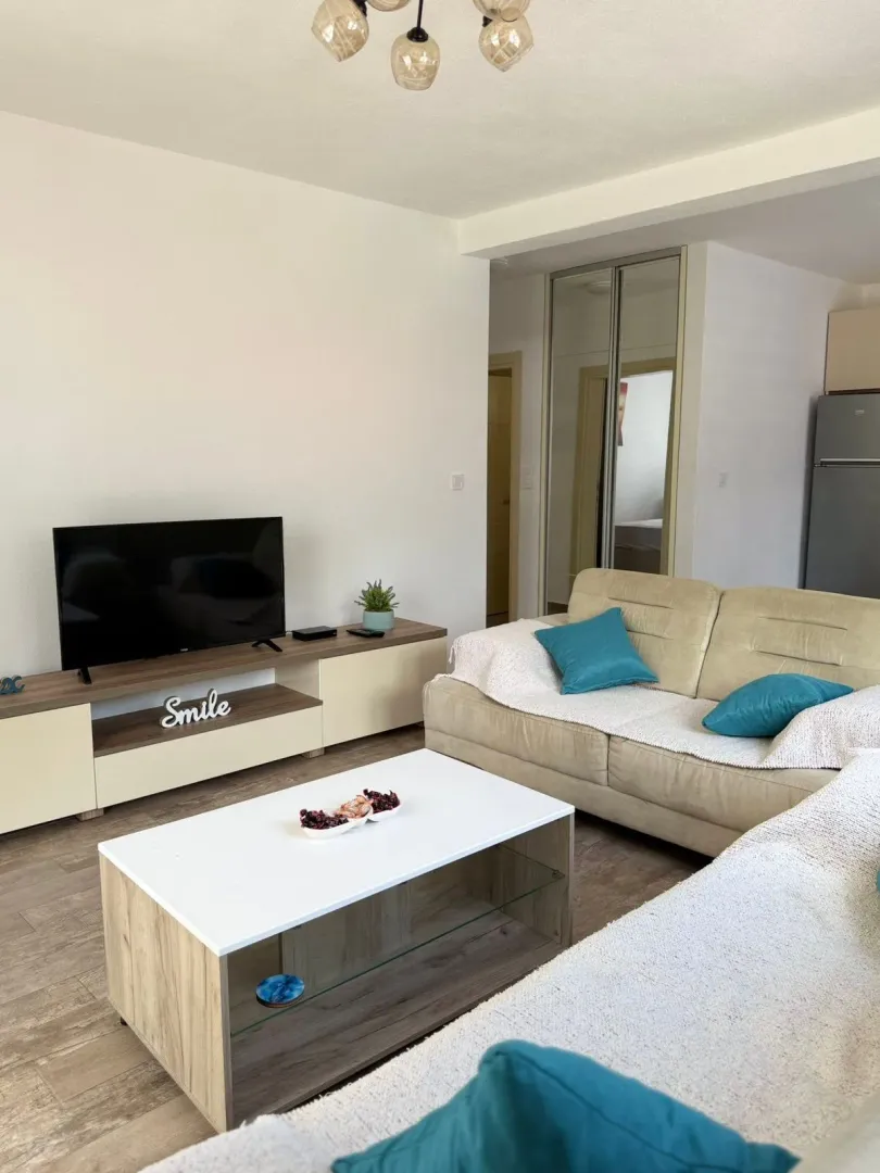 Dnevna soba sa garniturom, stočićem i televizorom na komodi.