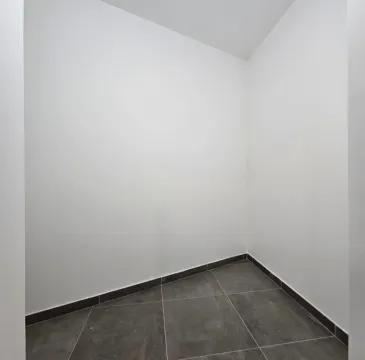 Prazna prostorija sa bijelim zidovima i tamnim pločicama na podu. - image 12
