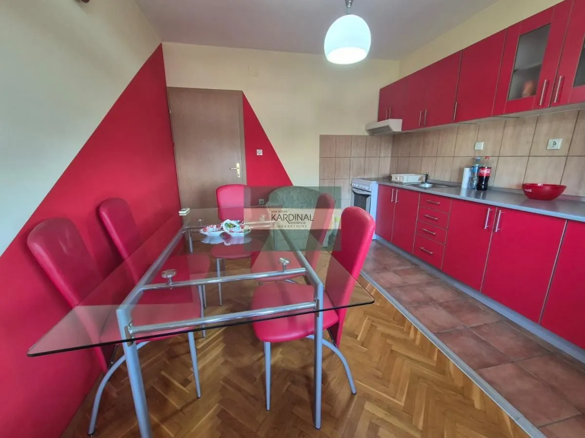 Kuhinja sa trpezarijom opremljena crvenim elementima i staklenim stolom.