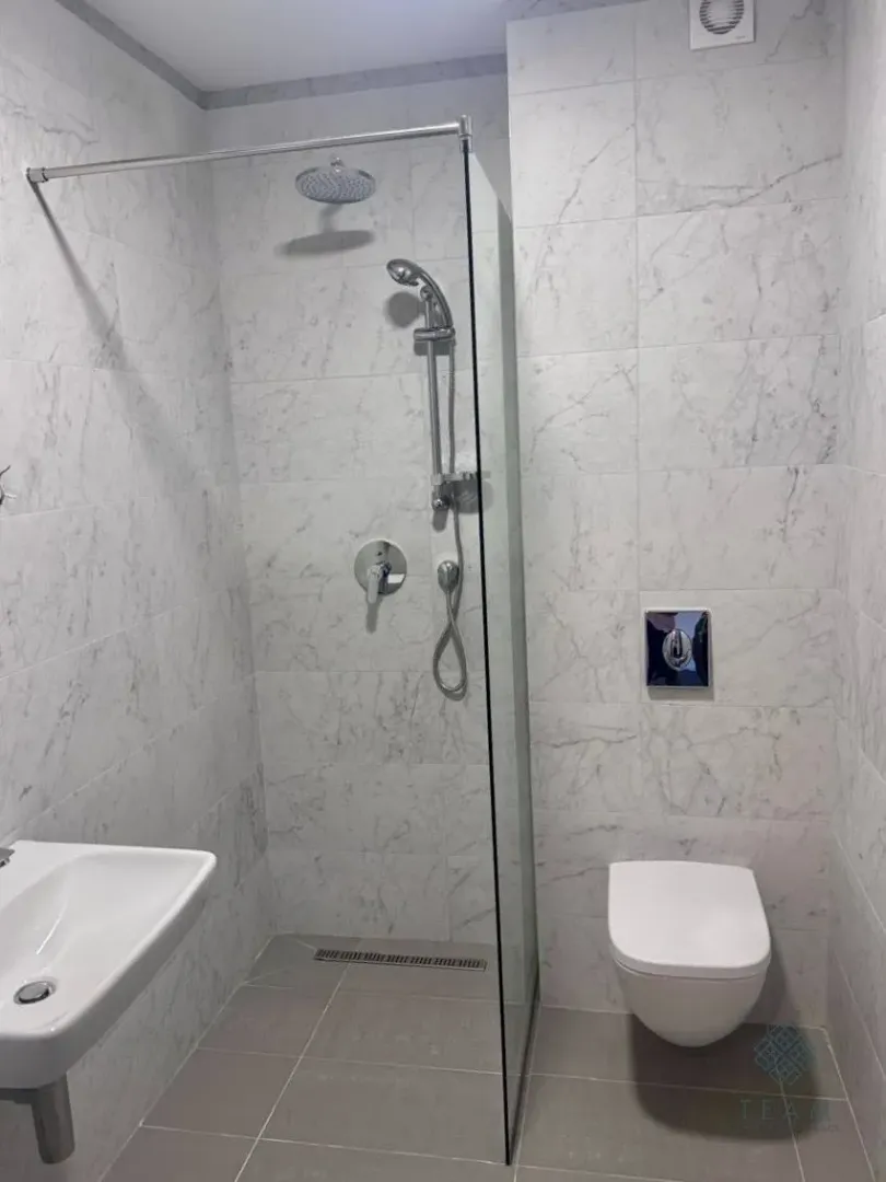 Moderne kupatilo sa tuš kabinom obloženom pločicama sa dezenom mermera.
