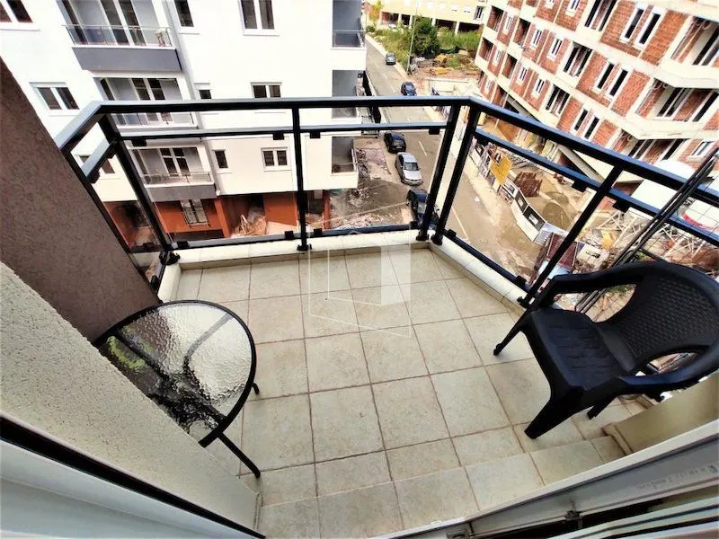 Manji popločani balkon sa crnom ogradom, stočićem i stolicom.