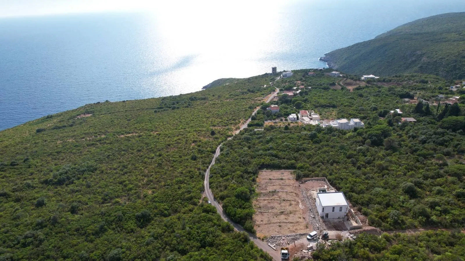 Pogled iz vazduha na priobalno područje sa zelenilom i putem koji vodi duž obale.