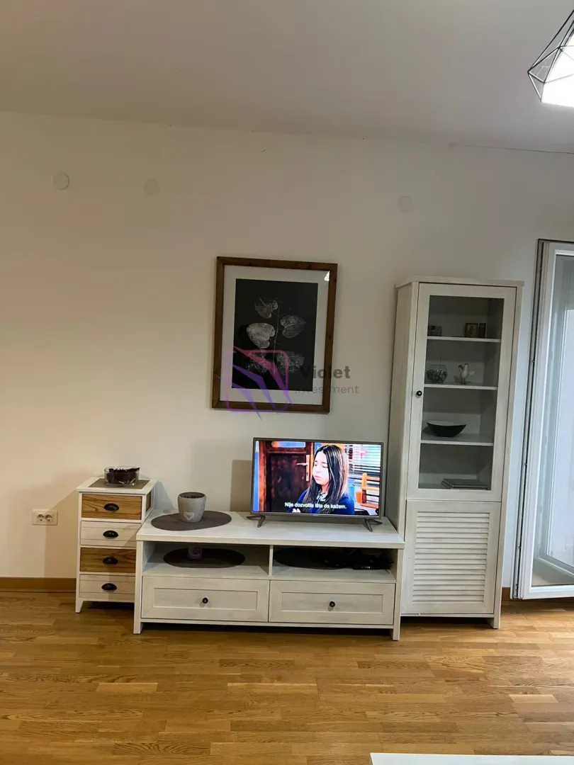 Dnevna soba sa belom komodom za TV, vitrinom i drvenim podom.