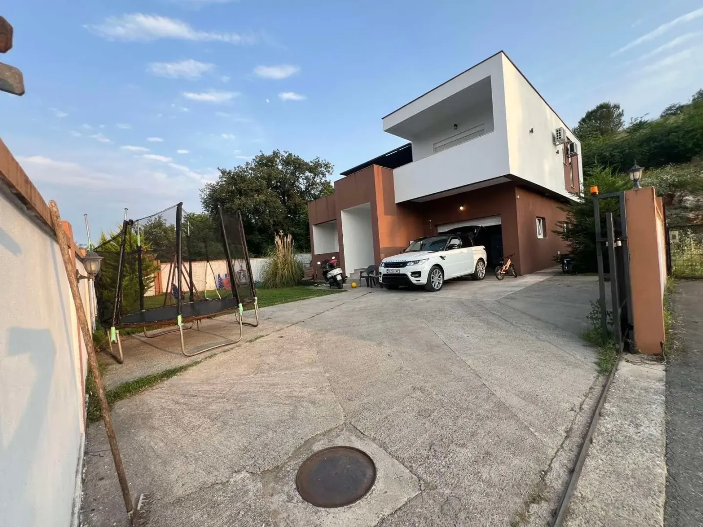 Pogled na dvorište i spoljašnjost kuće sa parkingom i igralištem.