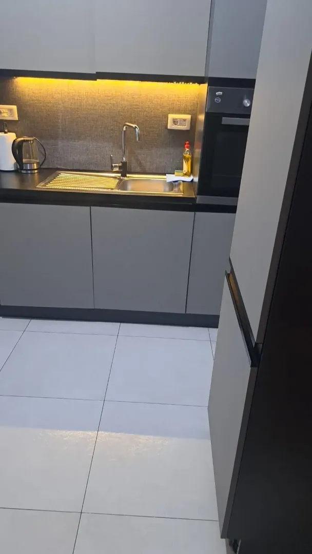 Moderna kuhinja sa sudoperom, ugradnom rernom i elementima u sivoj boji.