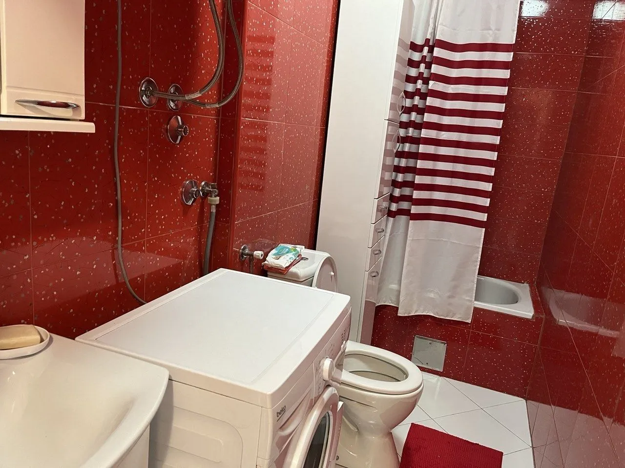 A bathroom with red tiles, a washing machine, and a bathtub.