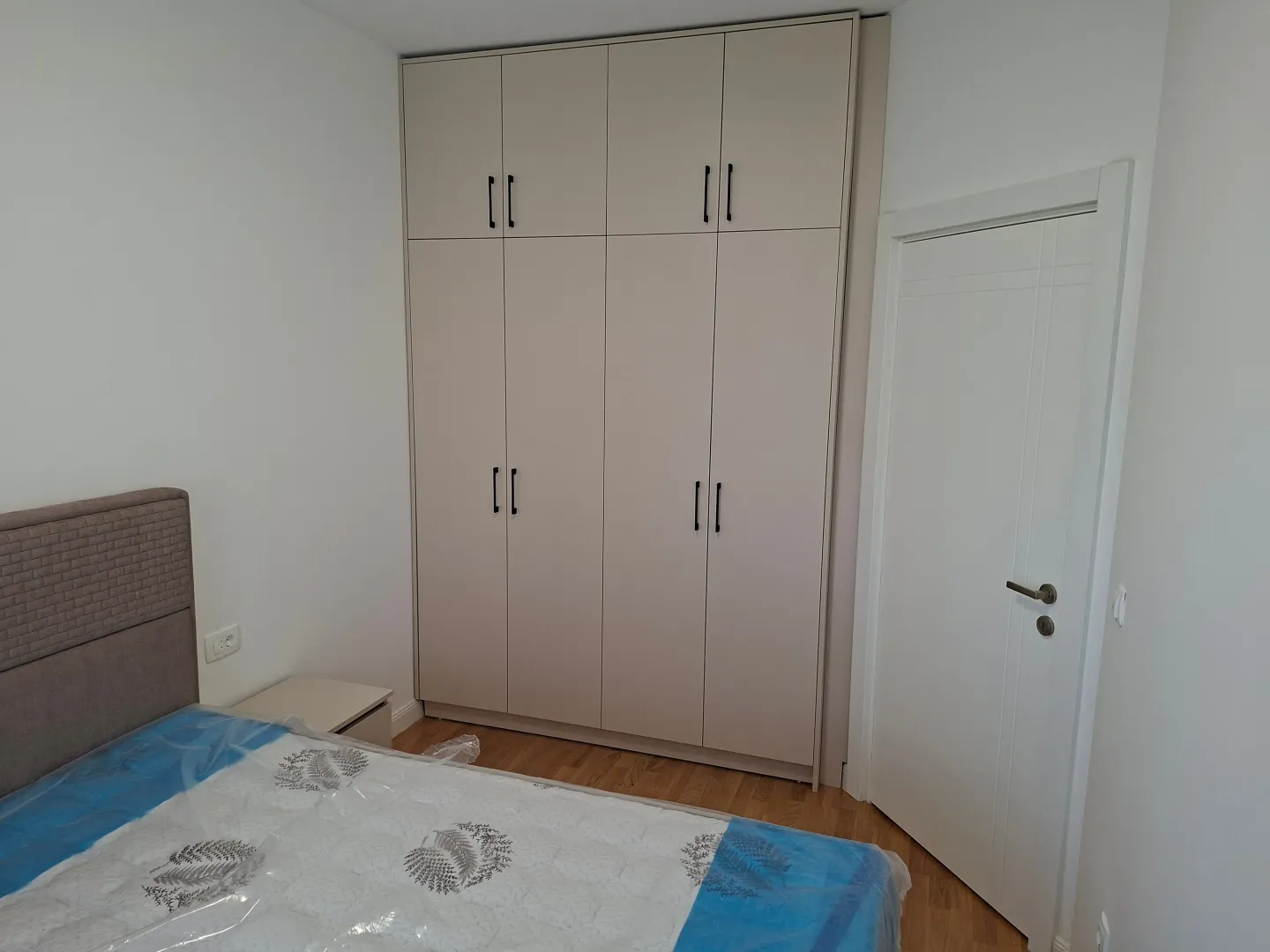 Bedroom with a double bed, large built-in wardrobe, and a white door.
