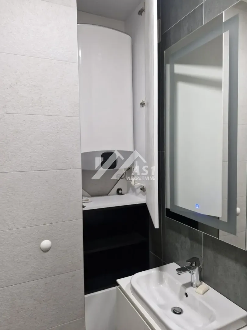 Kupatilo sa umivaonikom, ogledalom i ugrađenim bojlerom u ormariću.